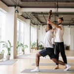 Instructor guides student in yoga pose in bright, modern studio.